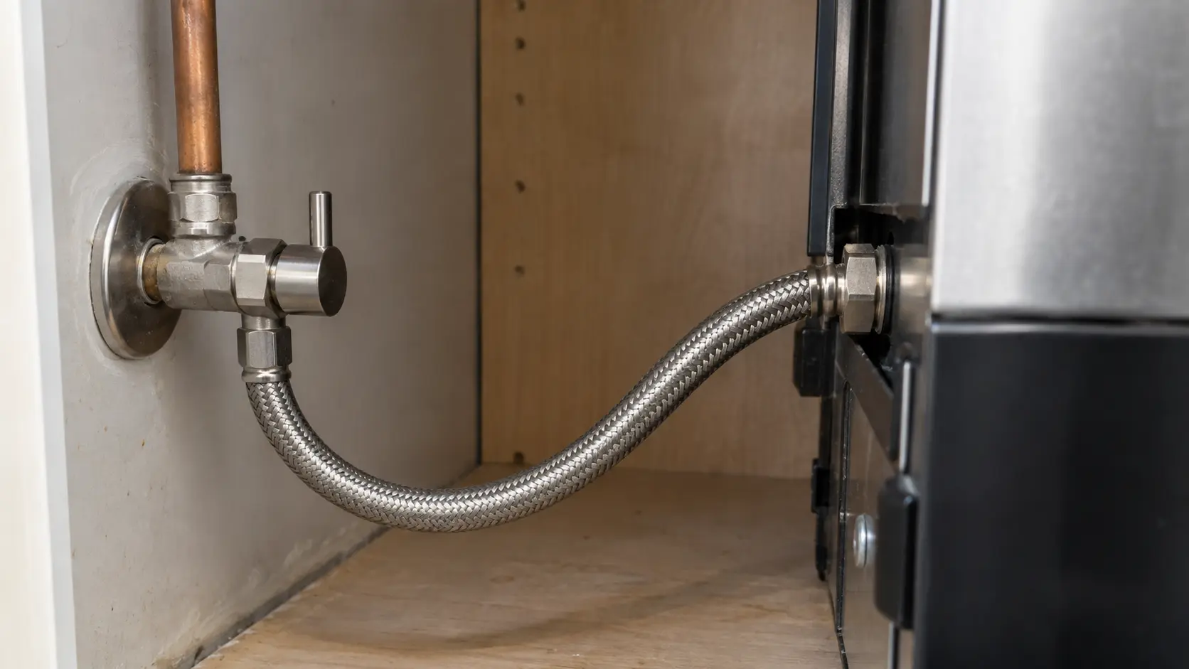 Close on a braided water line and shutoff valve behind the cabinet of a built-in coffee machine.