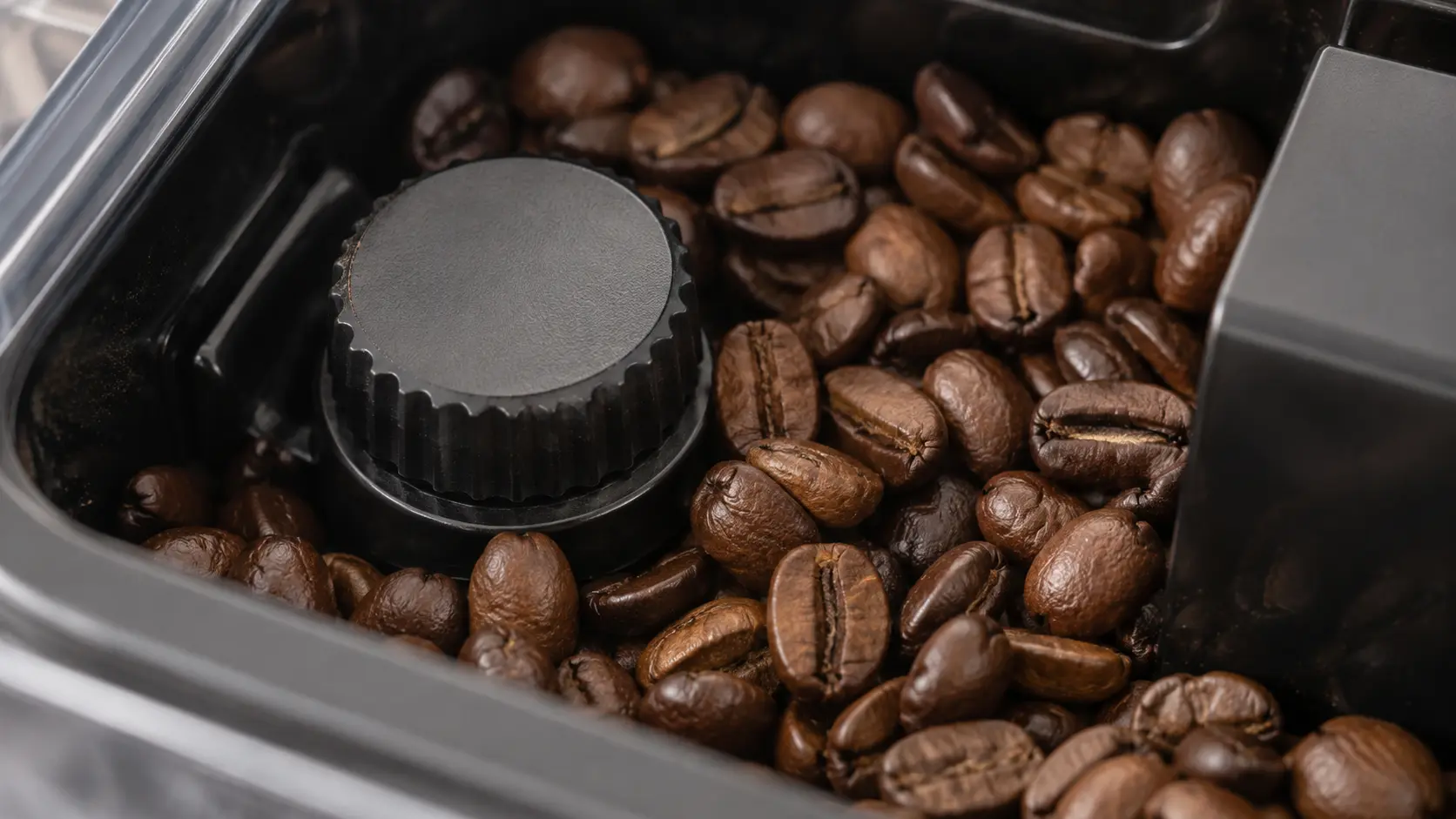 Close on the grind setting dial inside the bean hopper of a coffee machine, beans around it.